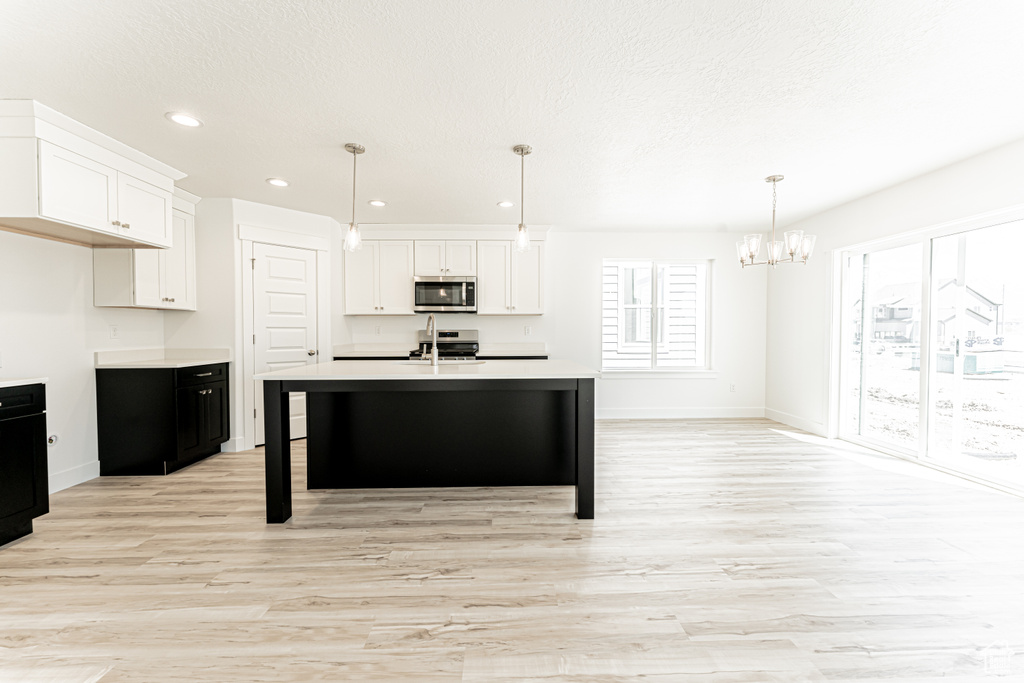 Kitchen with appliances with stainless steel finishes, a chandelier, light wood finished floors, light countertops, and white cabinetry