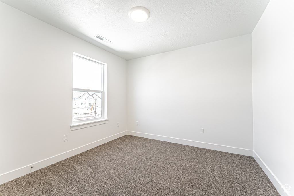 Empty room featuring dark carpet, a textured ceiling, and baseboards
