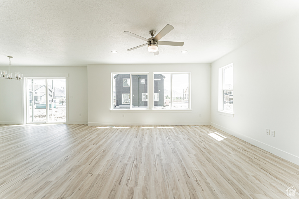 Unfurnished living room with a chandelier, light wood-style floors, ceiling fan, baseboards, and a textured ceiling