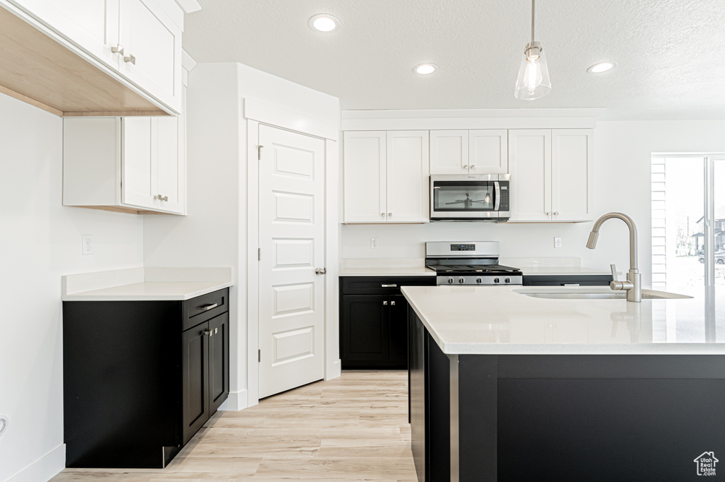 Kitchen with appliances with stainless steel finishes, a sink, light countertops, light wood finished floors, and white cabinets