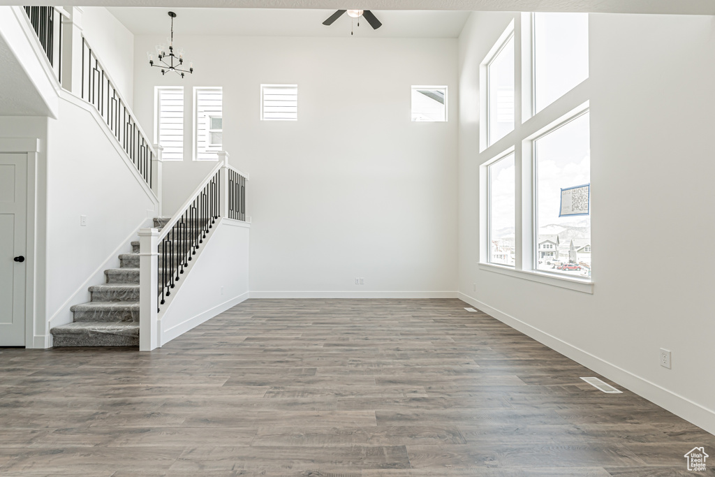 Unfurnished living room featuring ceiling fan, stairway, a high ceiling, baseboards, and a chandelier