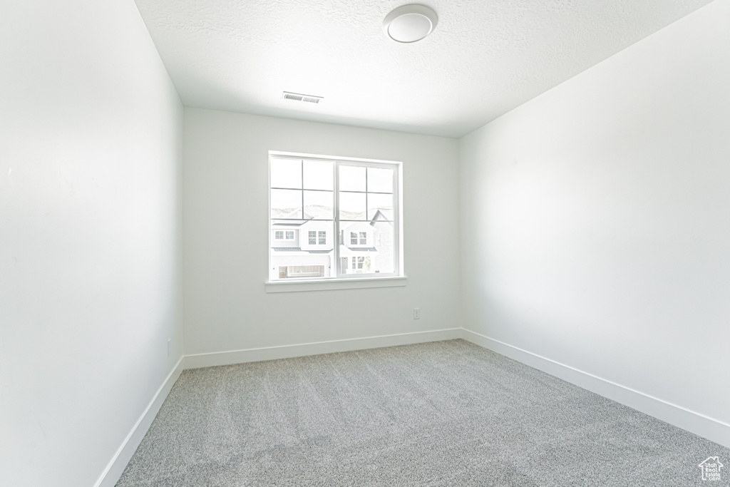 Empty room with carpet floors, baseboards, and a textured ceiling