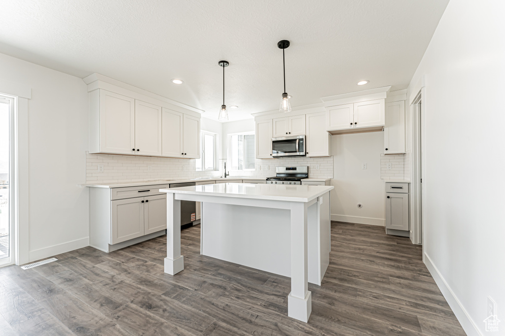 Kitchen with stainless steel appliances, decorative backsplash, light countertops, white cabinets, and a center island