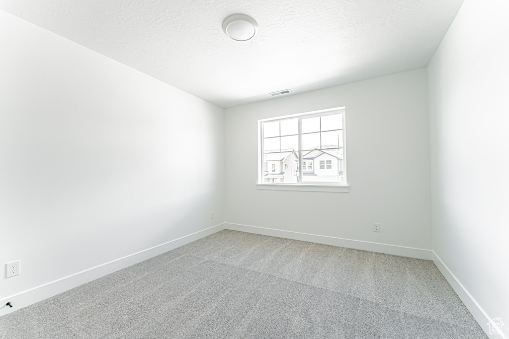 Empty room with light colored carpet, baseboards, and a textured ceiling