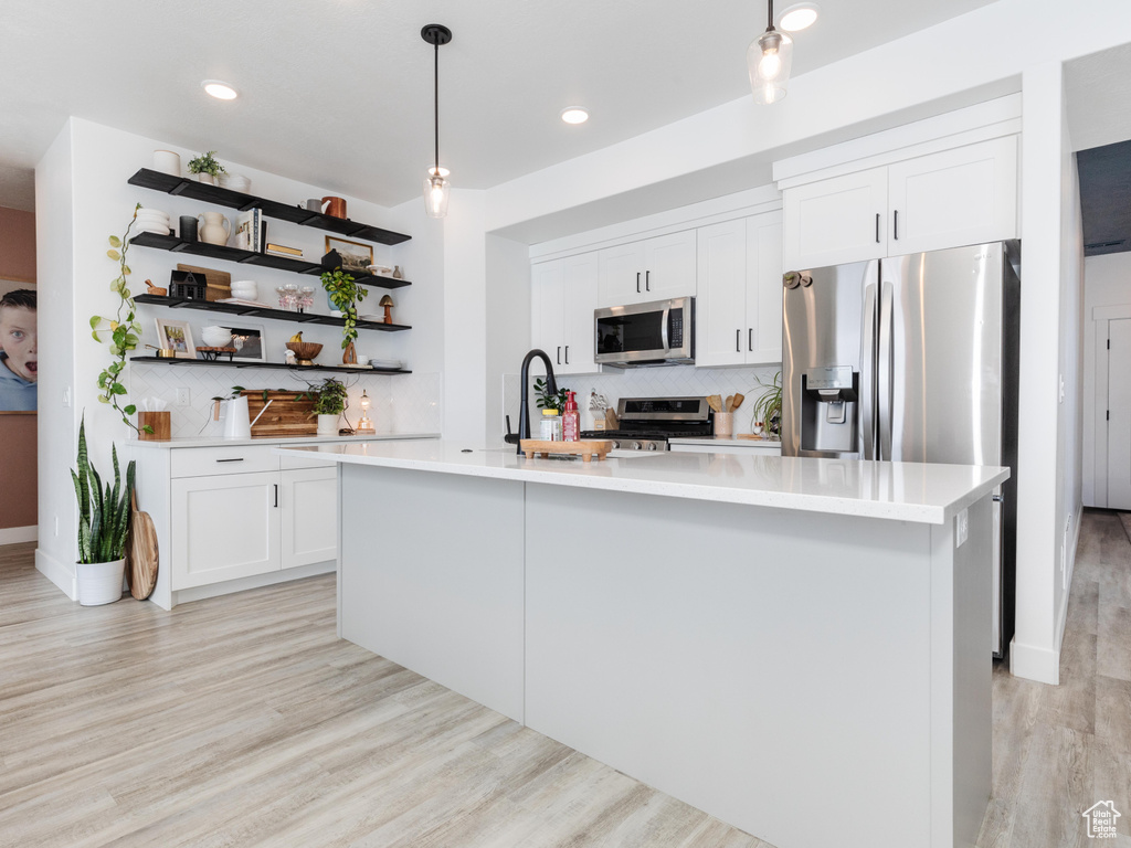 Kitchen featuring stainless steel appliances, white cabinetry, light countertops, a center island with sink, and pendant lighting