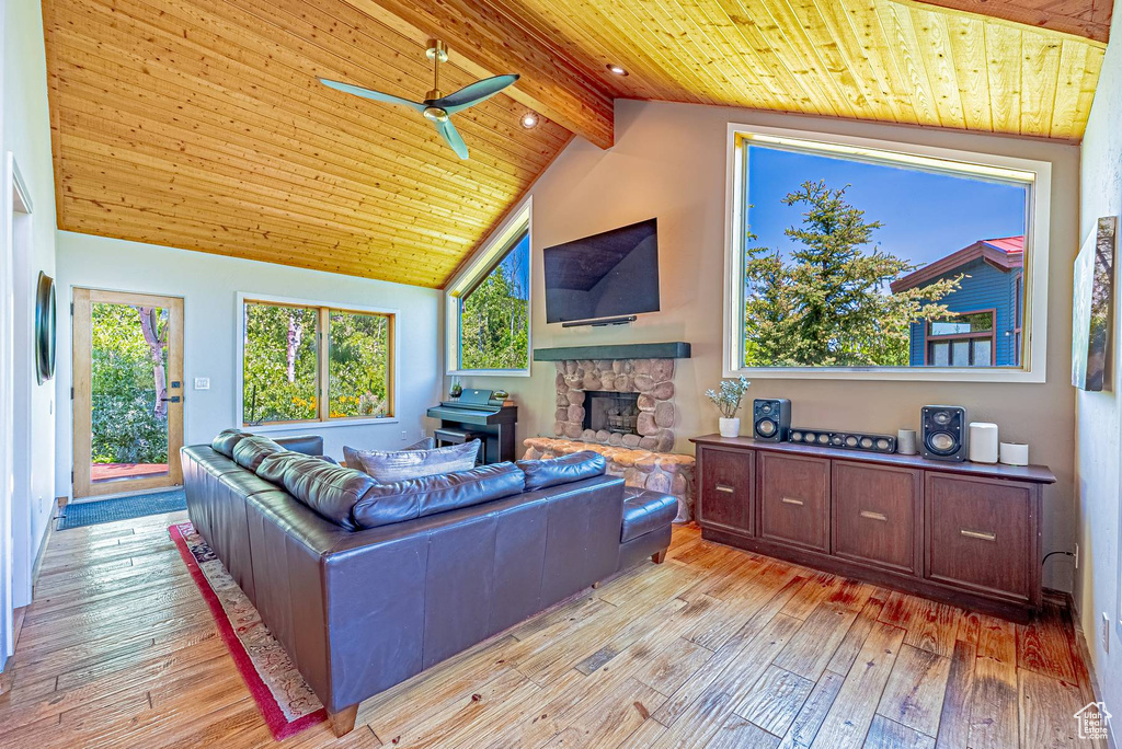 Living room featuring wood ceiling with exposed beams, a ceiling fan, light wood-style floors, a stone fireplace, and high vaulted ceiling