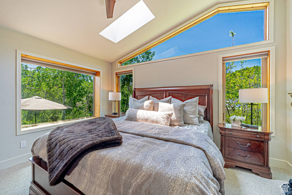 Carpeted bedroom with a skylight, baseboards, high vaulted ceiling, and a ceiling fan