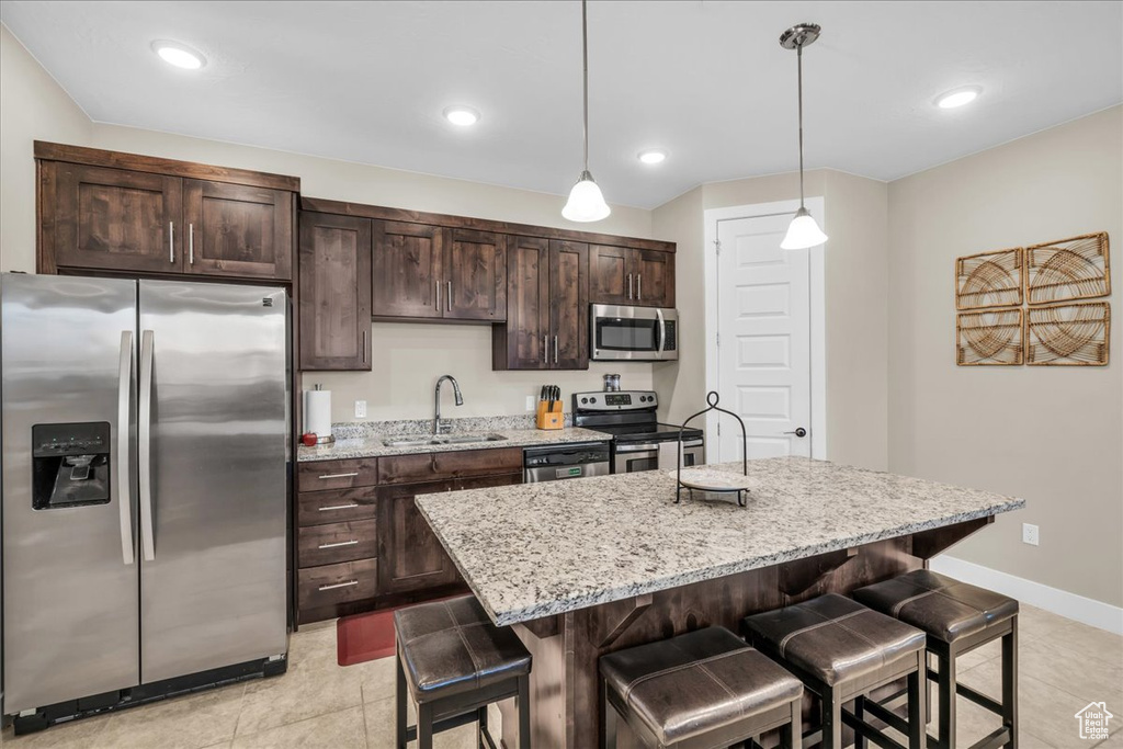 Kitchen with appliances with stainless steel finishes, a kitchen breakfast bar, light stone countertops, a kitchen island with sink, and a sink