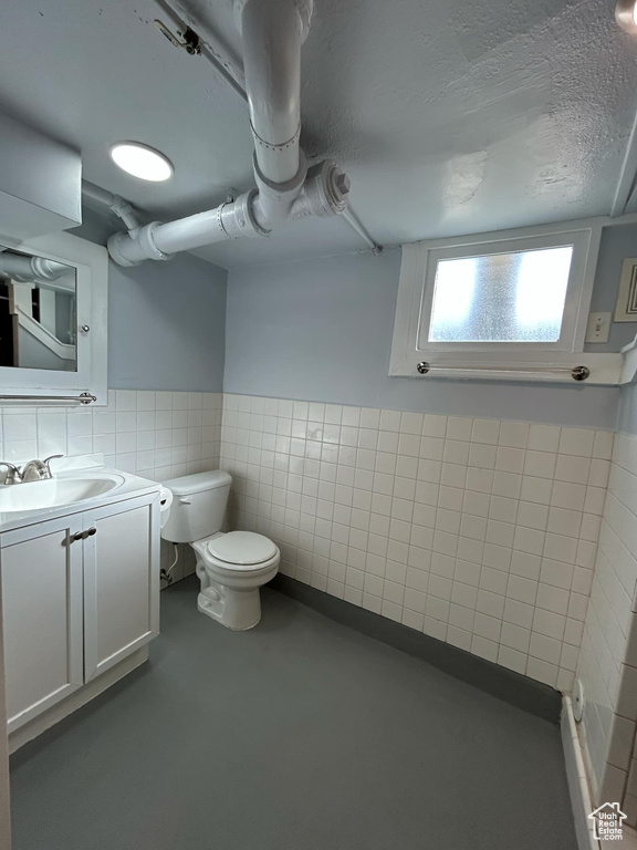 Bathroom featuring vanity, a wainscoted wall, a textured ceiling, tile walls, and toilet