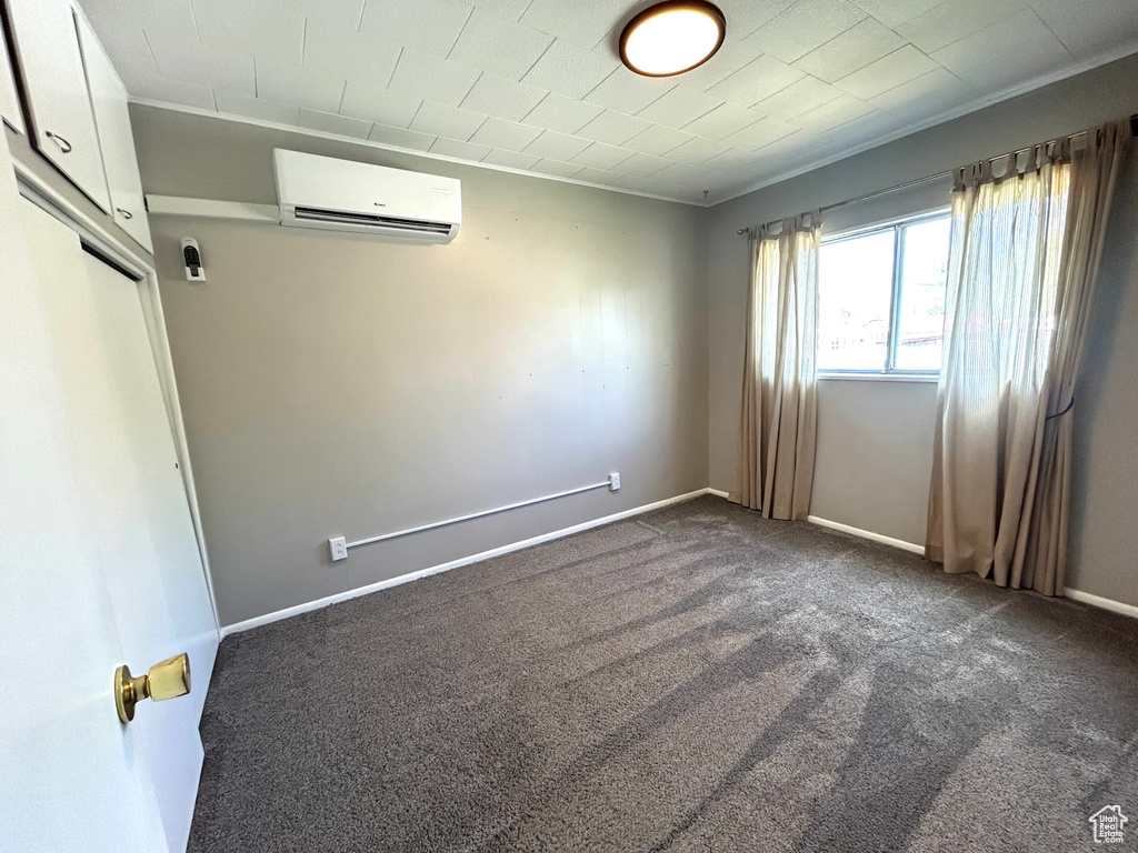 Spare room with a wall mounted AC, baseboards, and dark carpet