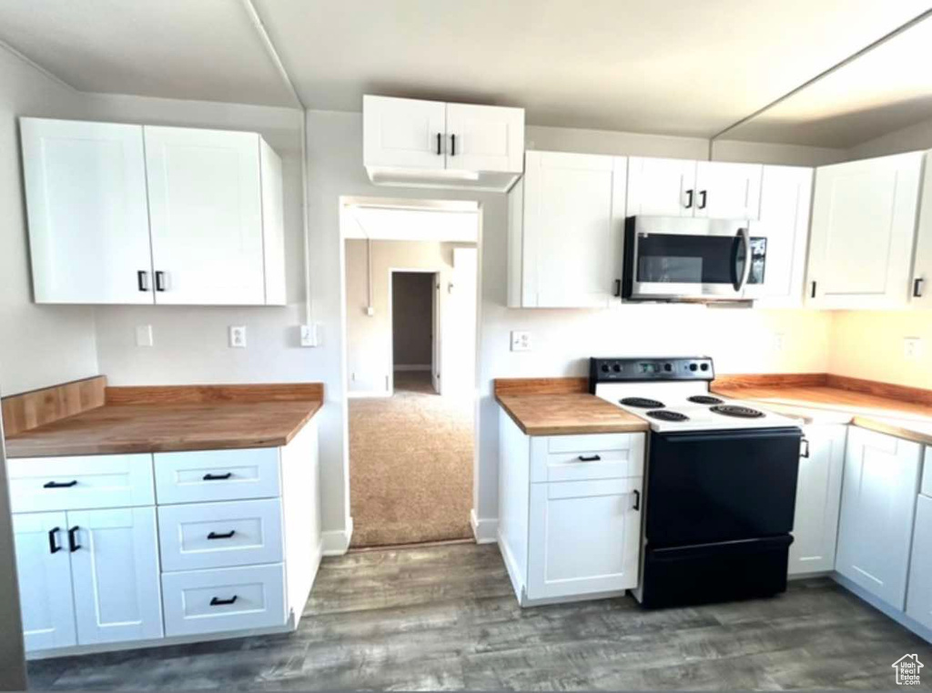 Kitchen featuring electric range, white cabinets, wooden counters, dark wood-style floors, and stainless steel microwave