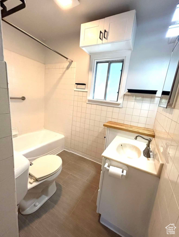 Full bath with toilet, shower / bathing tub combination, vanity, and tile walls