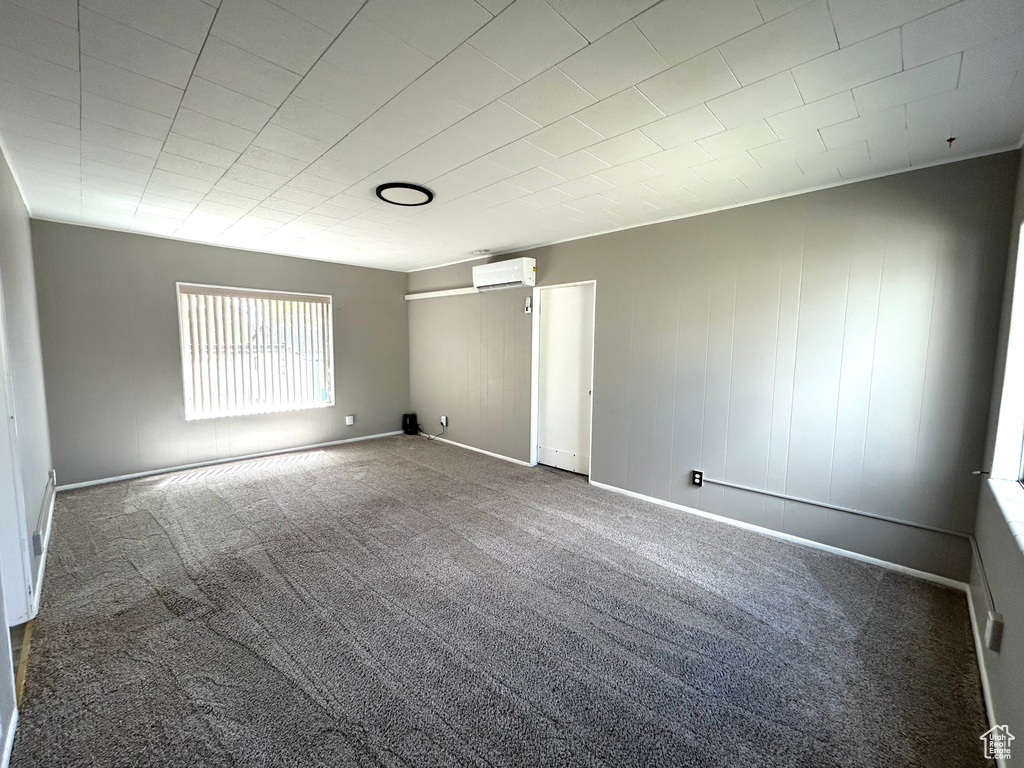 Carpeted empty room with an AC wall unit and baseboards