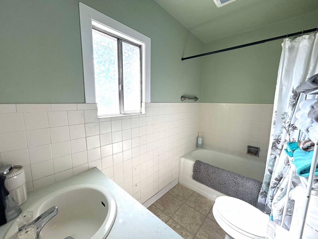 Full bathroom featuring toilet, a tub, tile patterned floors, a sink, and tile walls