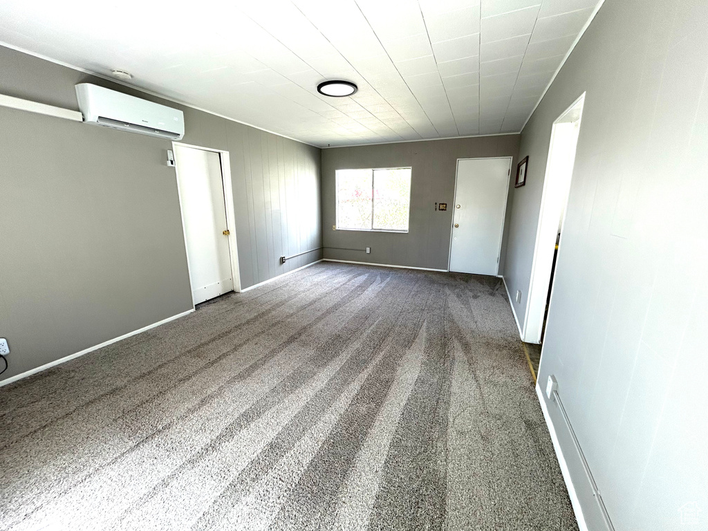 Unfurnished room featuring a wall mounted AC, baseboards, and carpet