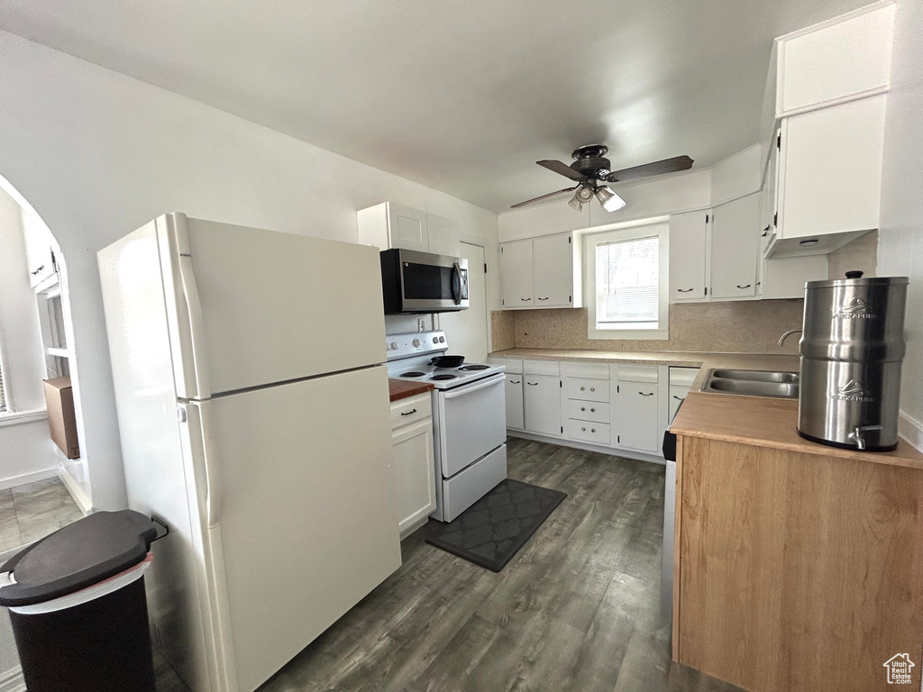 Kitchen with a ceiling fan, a sink, white cabinets, dark wood-style flooring, and white appliances