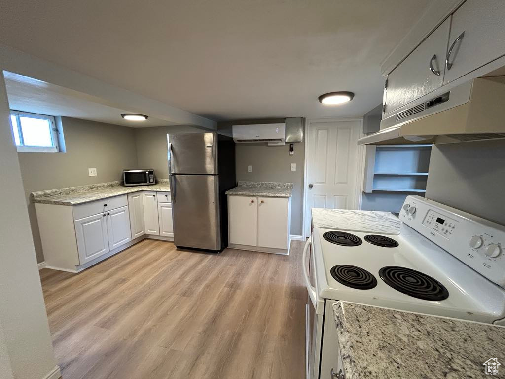 Kitchen with a wall mounted AC, stainless steel appliances, white cabinets, light wood-style floors, and under cabinet range hood