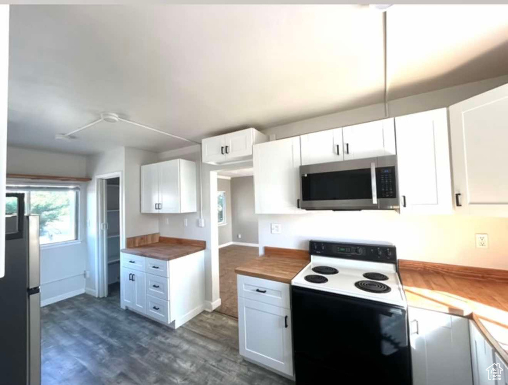 Kitchen featuring electric range, white cabinets, dark wood finished floors, wood counters, and stainless steel microwave