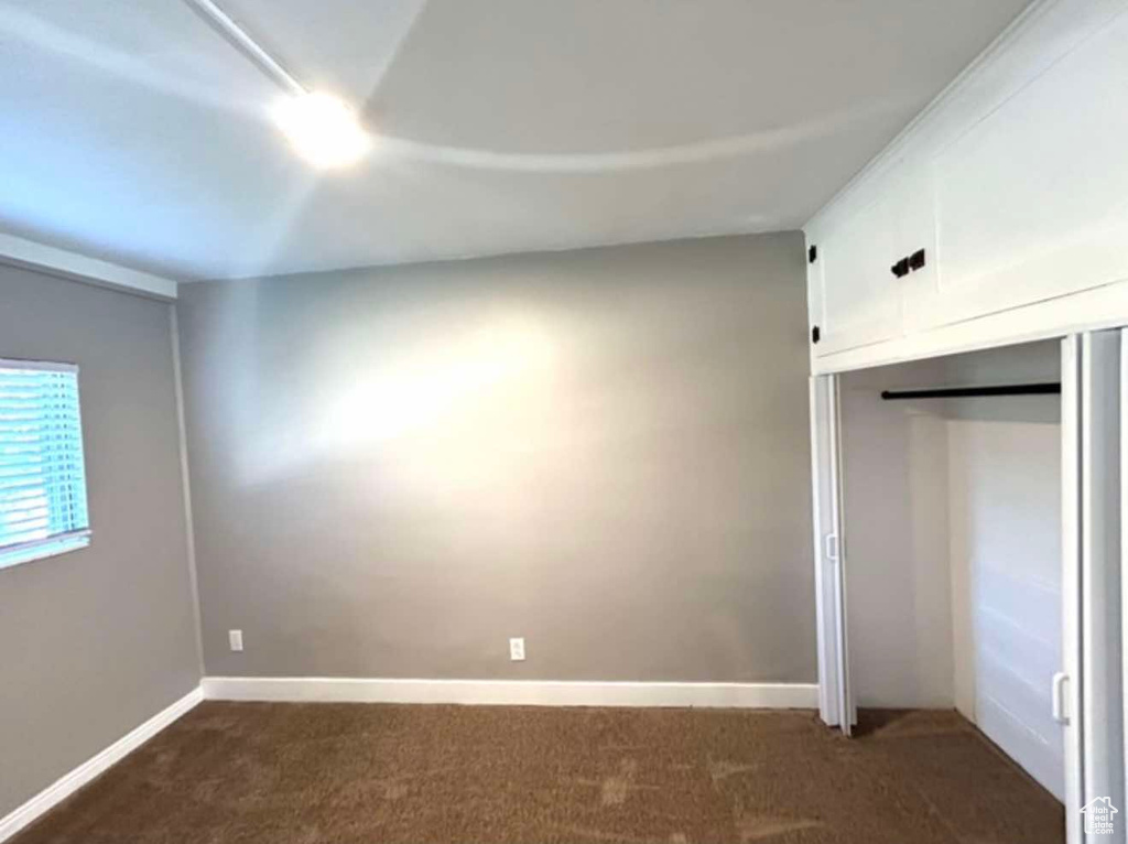 Unfurnished bedroom featuring baseboards, dark colored carpet, and a closet