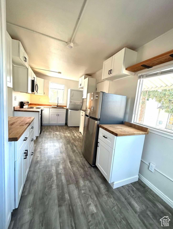 Kitchen with wooden counters, stacked washing maching and dryer, white cabinetry, and stainless steel appliances