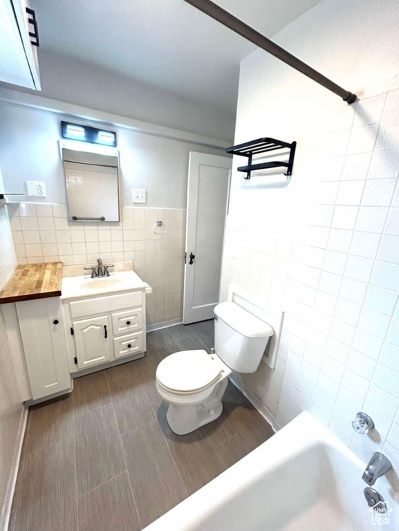 Bathroom with tile walls, toilet, wainscoting, tub / shower combination, and vanity