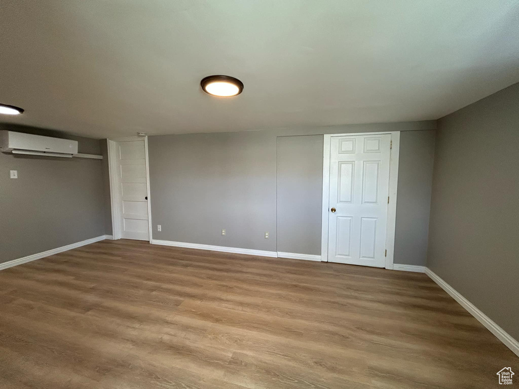 Interior space with a wall mounted air conditioner, baseboards, and wood finished floors