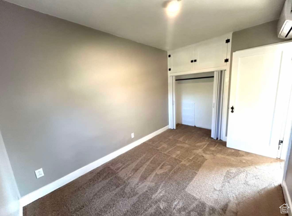 Unfurnished bedroom with carpet, baseboards, a closet, and a wall mounted air conditioner