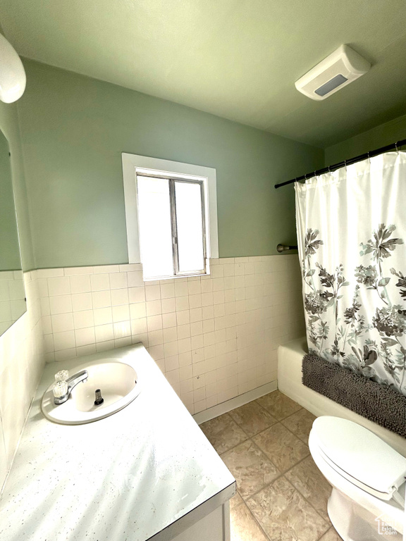 Full bathroom with tile walls, toilet, wainscoting, shower / bath combination with curtain, and vanity
