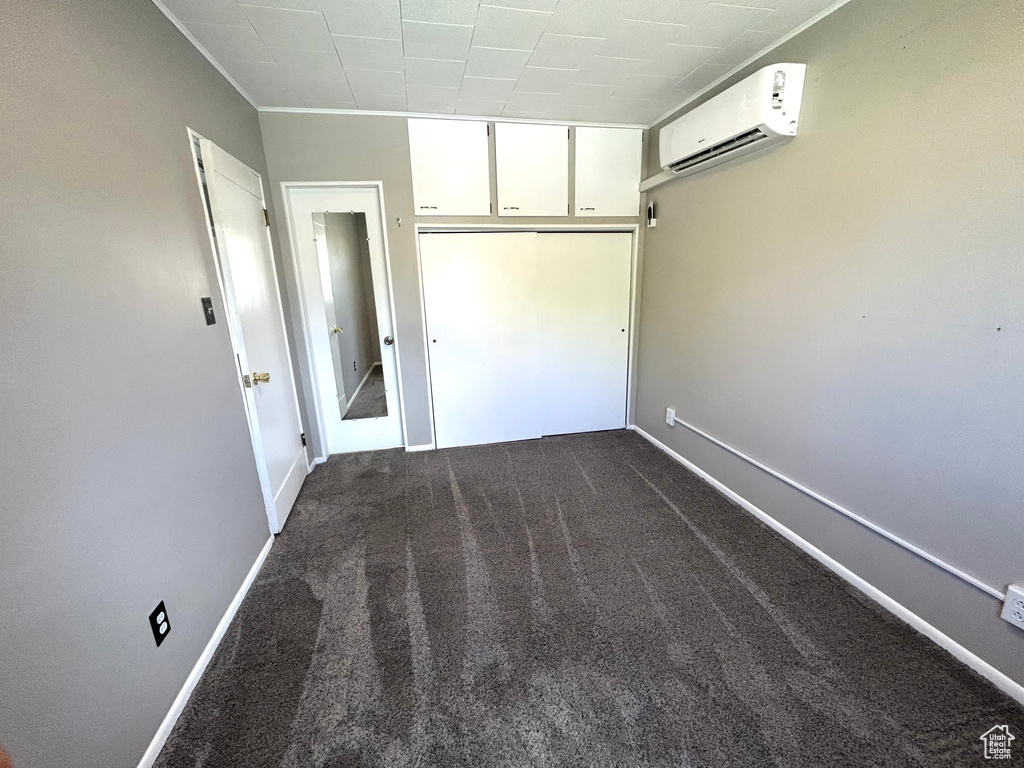 Unfurnished bedroom featuring a wall mounted air conditioner, dark colored carpet, and baseboards