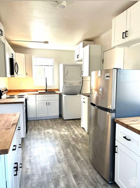 Kitchen featuring stacked washer and dryer, white cabinets, appliances with stainless steel finishes, wooden counters, and a sink