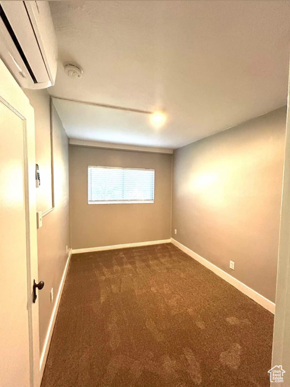 Spare room featuring dark colored carpet, a wall mounted air conditioner, and baseboards