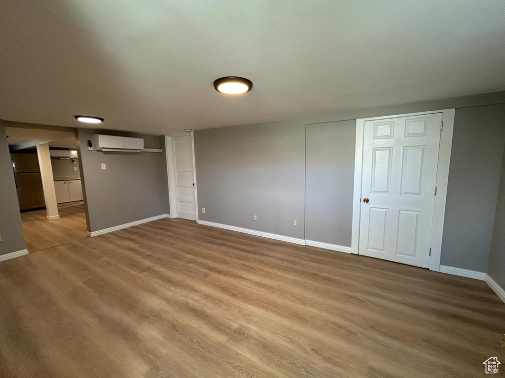 Finished below grade area with light wood-style flooring, baseboards, and a wall mounted air conditioner