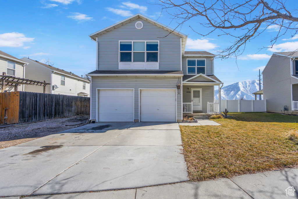 Traditional-style home with a mountain view, a garage, fence, concrete driveway, and a front lawn