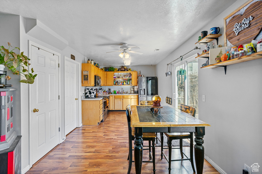 Dining room featuring light wood-style floors, a textured ceiling, baseboards, and a ceiling fan