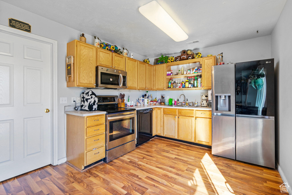 Kitchen with appliances with stainless steel finishes, light countertops, light wood-type flooring, open shelves, and a sink