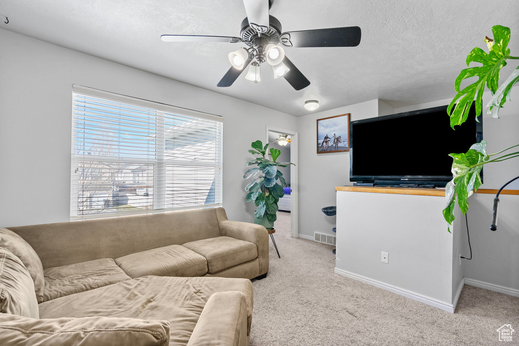 Living room with a textured ceiling, light colored carpet, a ceiling fan, baseboards, and visible vents