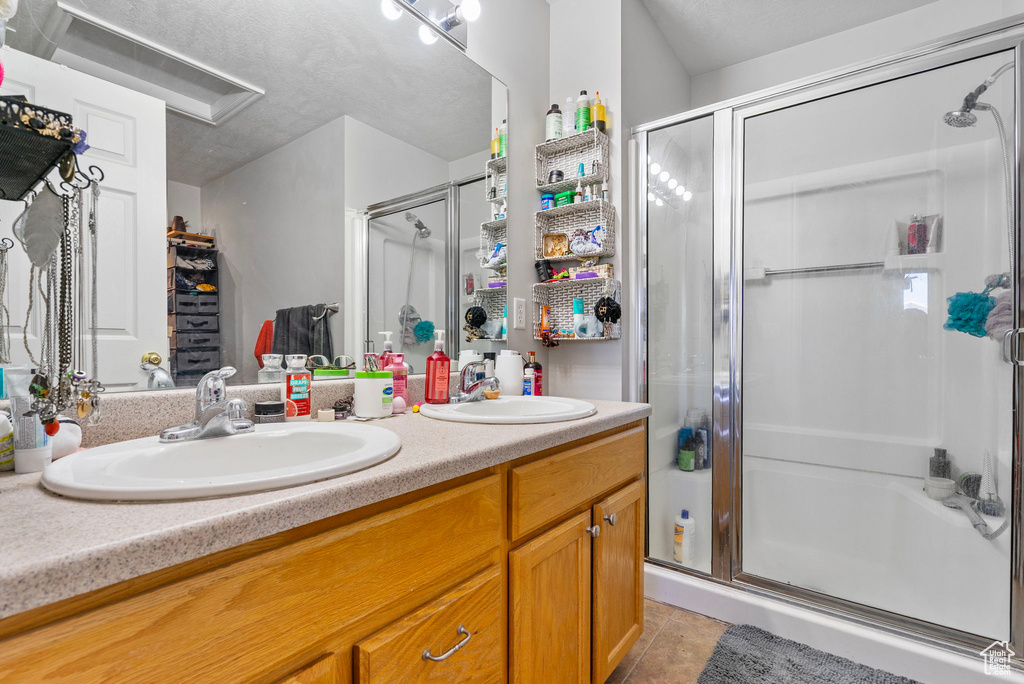 Full bathroom featuring double vanity, a stall shower, a sink, and tile patterned floors