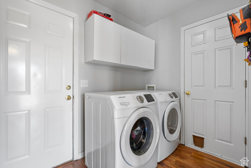 Washroom with dark wood finished floors, washing machine and dryer, and cabinet space