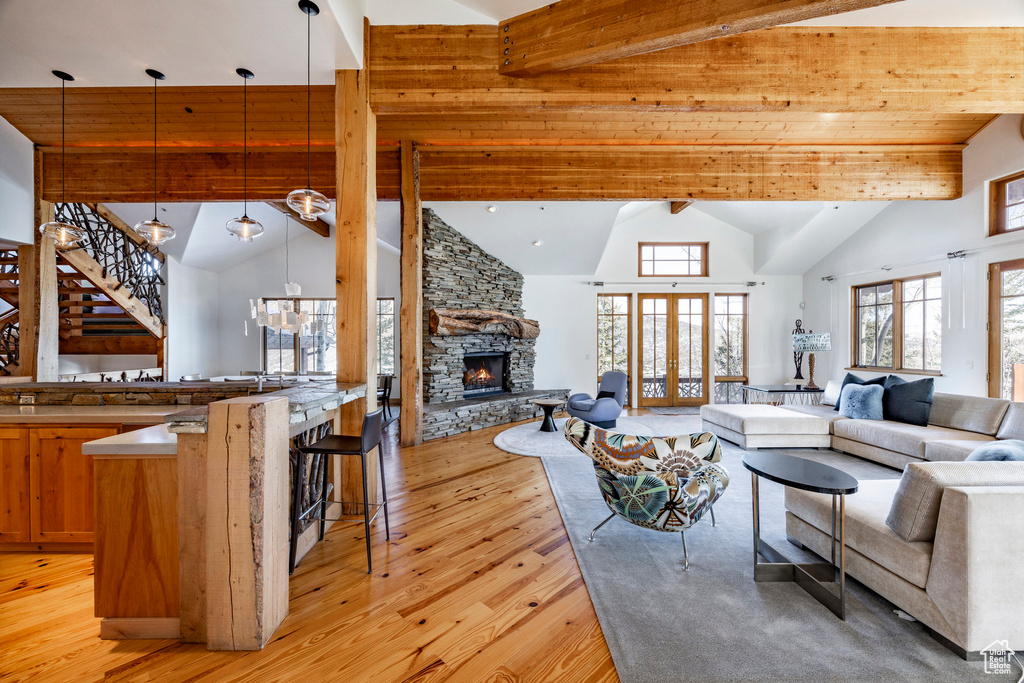 Living area featuring high vaulted ceiling, light wood-style floors, a stone fireplace, beam ceiling, and stairway