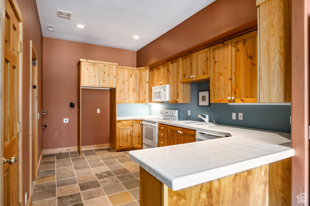 Kitchen featuring white appliances, dark stone finish flooring, baseboards, a peninsula, and tile counters