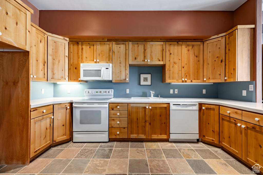 Kitchen with white appliances, a sink, and stone tile floors