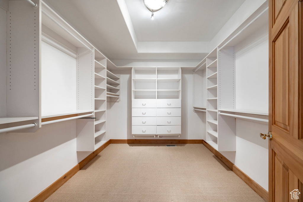Walk in closet with light carpet and a tray ceiling