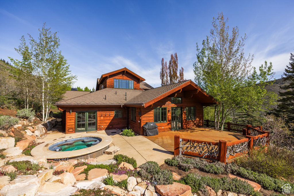 Rear view of property with an in-ground hot tub, a wooden deck, and a patio