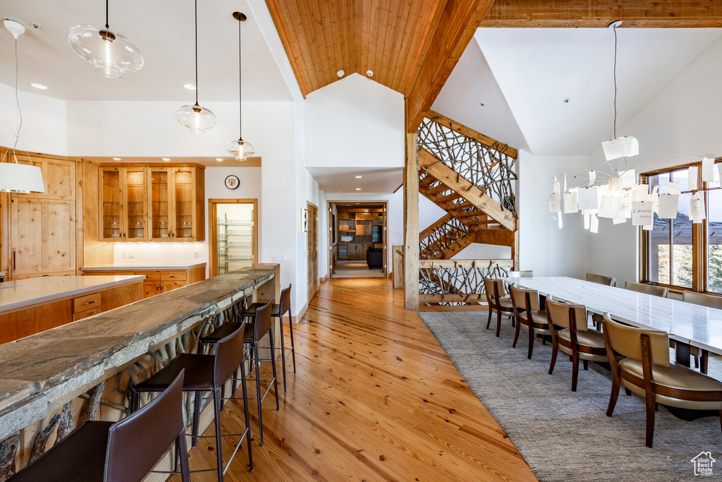 Dining room featuring high vaulted ceiling, bar, stairway, light wood-style flooring, and recessed lighting