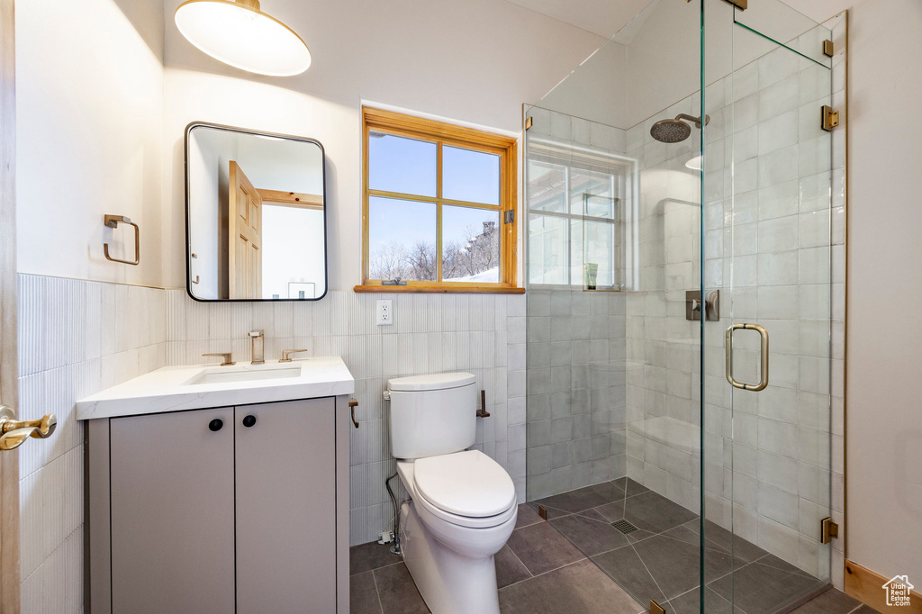 Bathroom featuring tile walls, vanity, a shower stall, toilet, and tile patterned floors