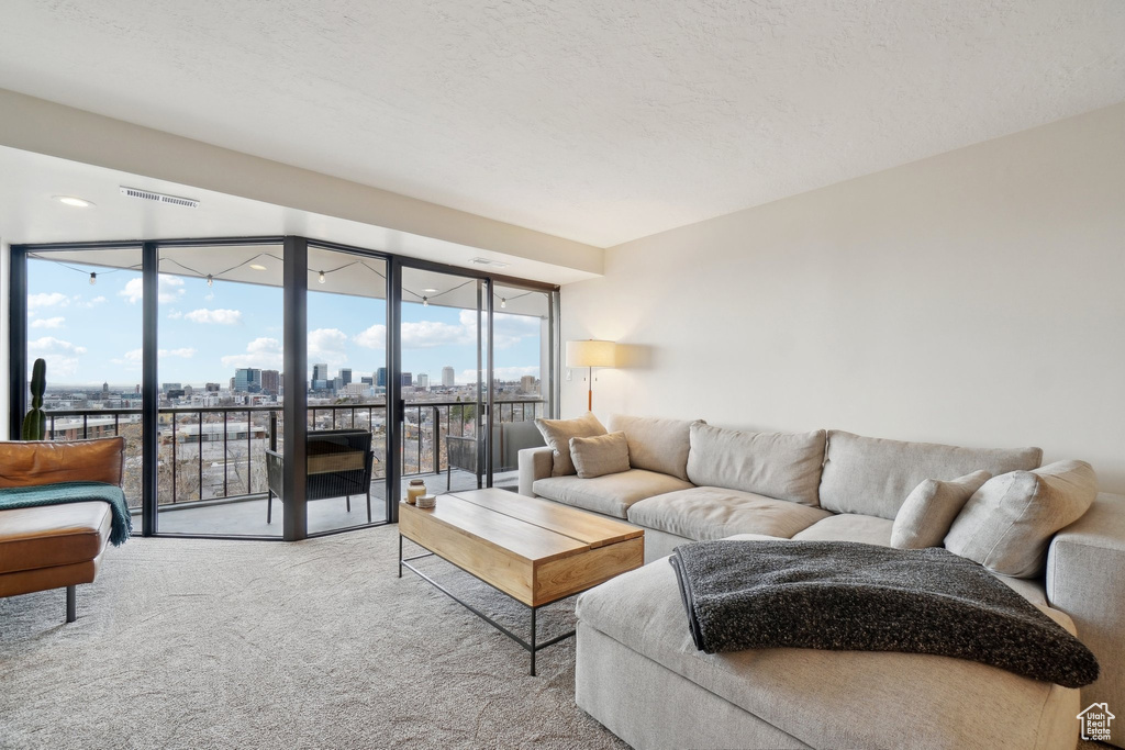 Living room featuring a textured ceiling, carpet floors, floor to ceiling windows, and a city view