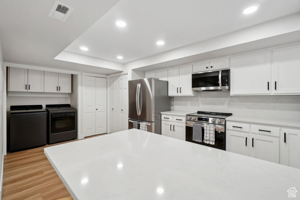 Kitchen with separate washer and dryer, visible vents, white cabinetry, light countertops, and appliances with stainless steel finishes