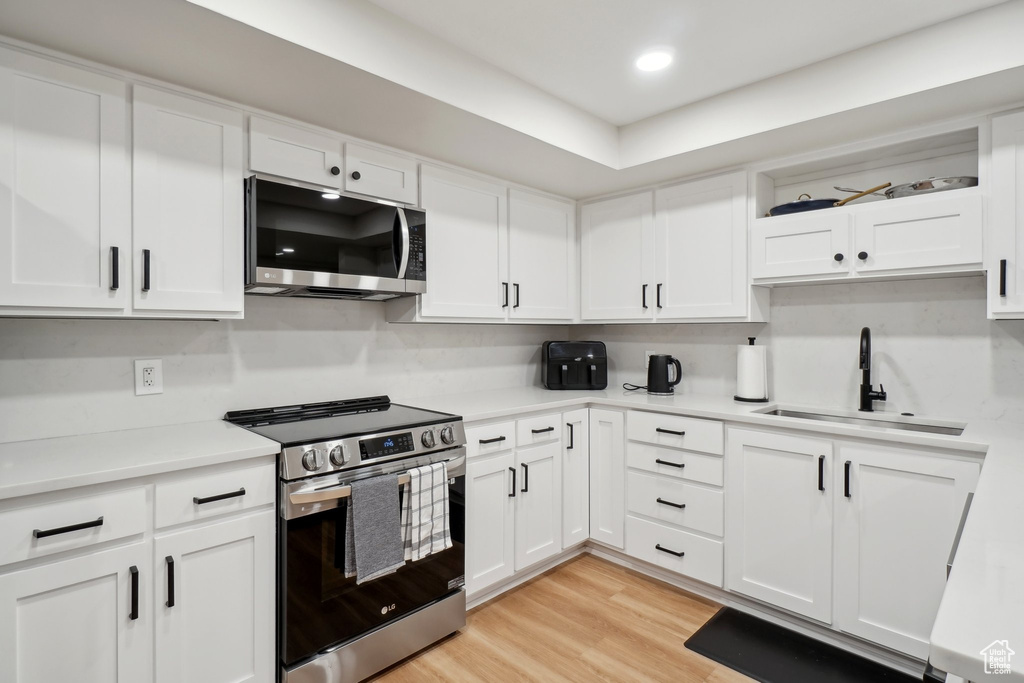 Kitchen featuring open shelves, stainless steel appliances, light countertops, white cabinets, and a sink