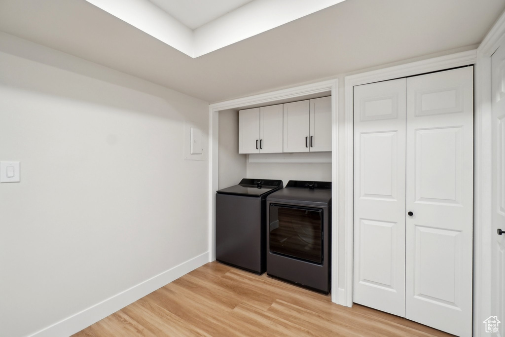 Clothes washing area with light wood-style flooring, washing machine and clothes dryer, cabinet space, and baseboards