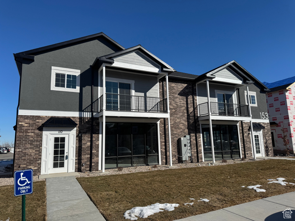 View of front of house with a balcony, stucco siding, a front lawn, and brick siding
